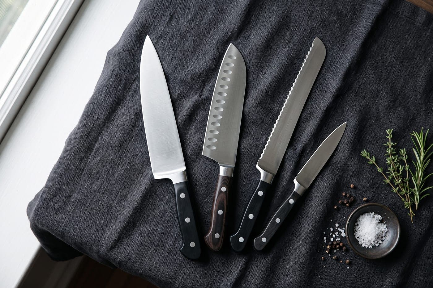 A spread of kitchen knives laid out on a dark linen cloth